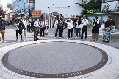 嘉義市政團隊參訪府中雙城計劃的重慶路口，用手機紀念下方鋪面特別的板橋歷史時間軸設計。