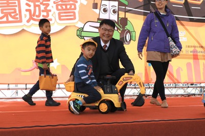 新北市副市長陳純敬在路平親子園遊會中和抽中迷你挖土機的小朋友合影